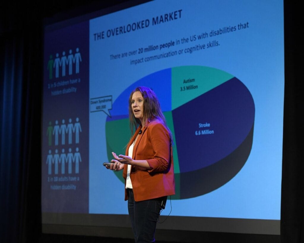 A woman standing on a stage in front of a projector giving a presentation