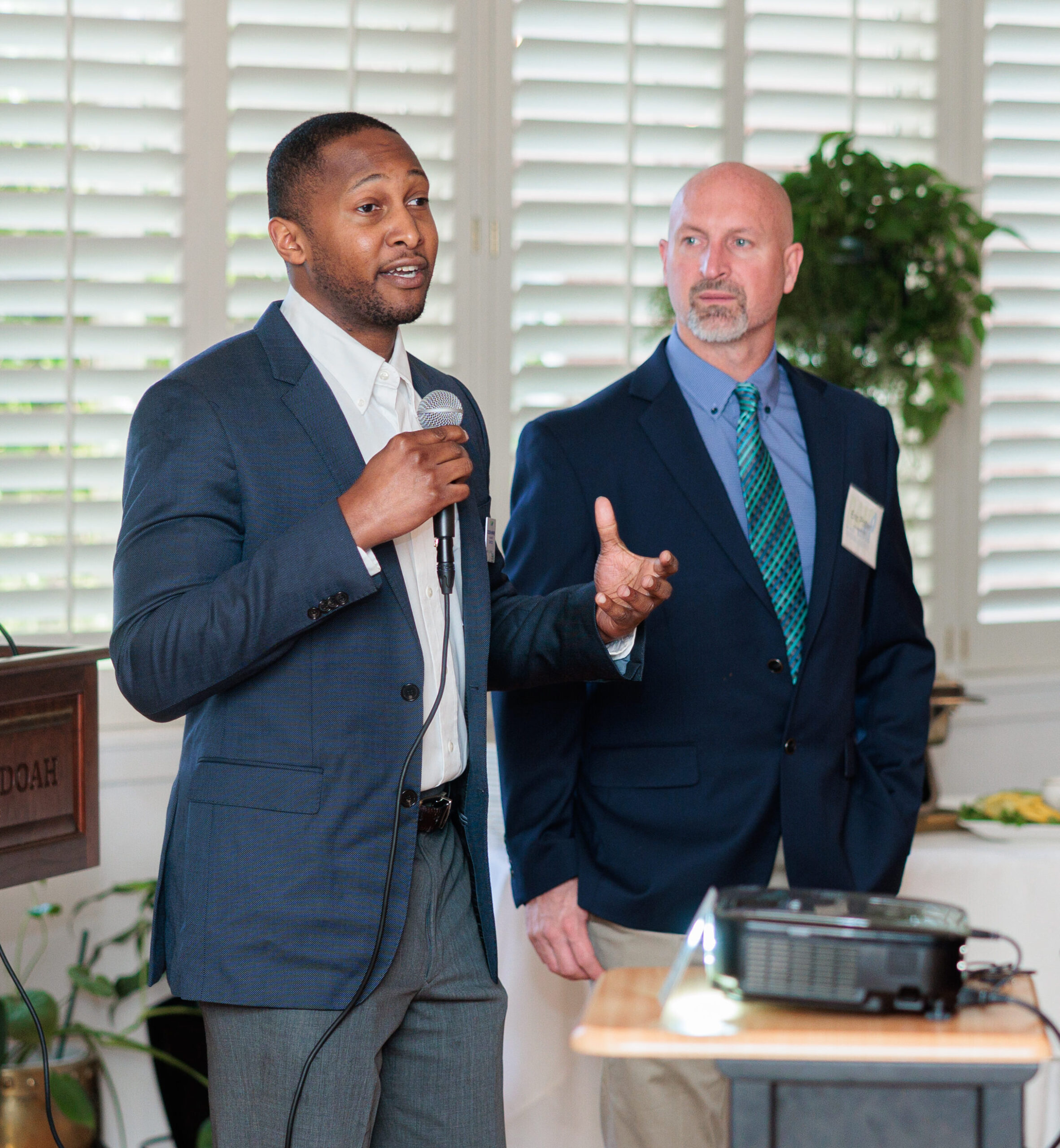A man speaking with a microphone to a room of people