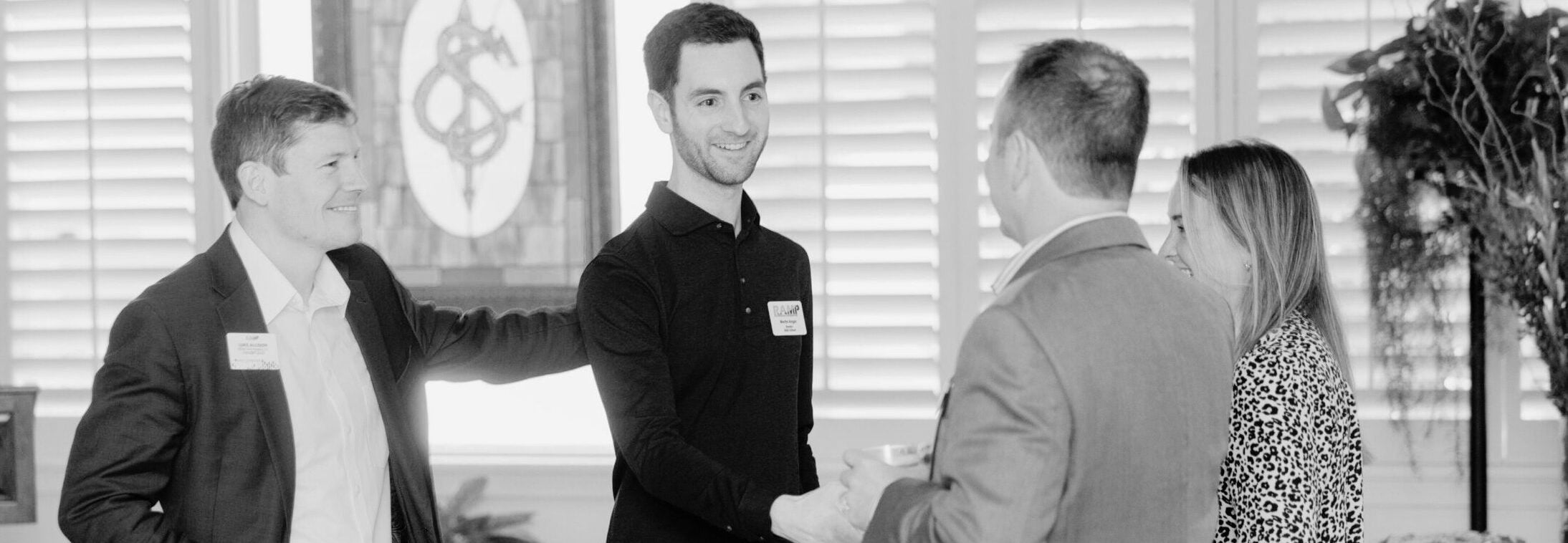 A black and white photo of 2 men shaking hands with other people standing around them